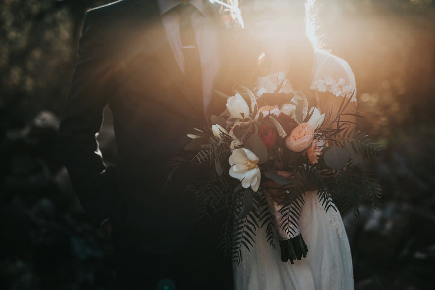 A bride and groom holding a bouquet at golden hour